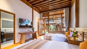 A hotel room with two beds, a wooden desk, a TV, and a balcony with a view of traditional architecture.