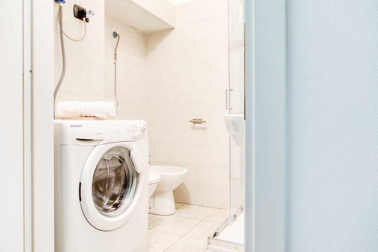 Une petite salle de bain équipée d’un lave-linge, de toilettes et d’une douche.
