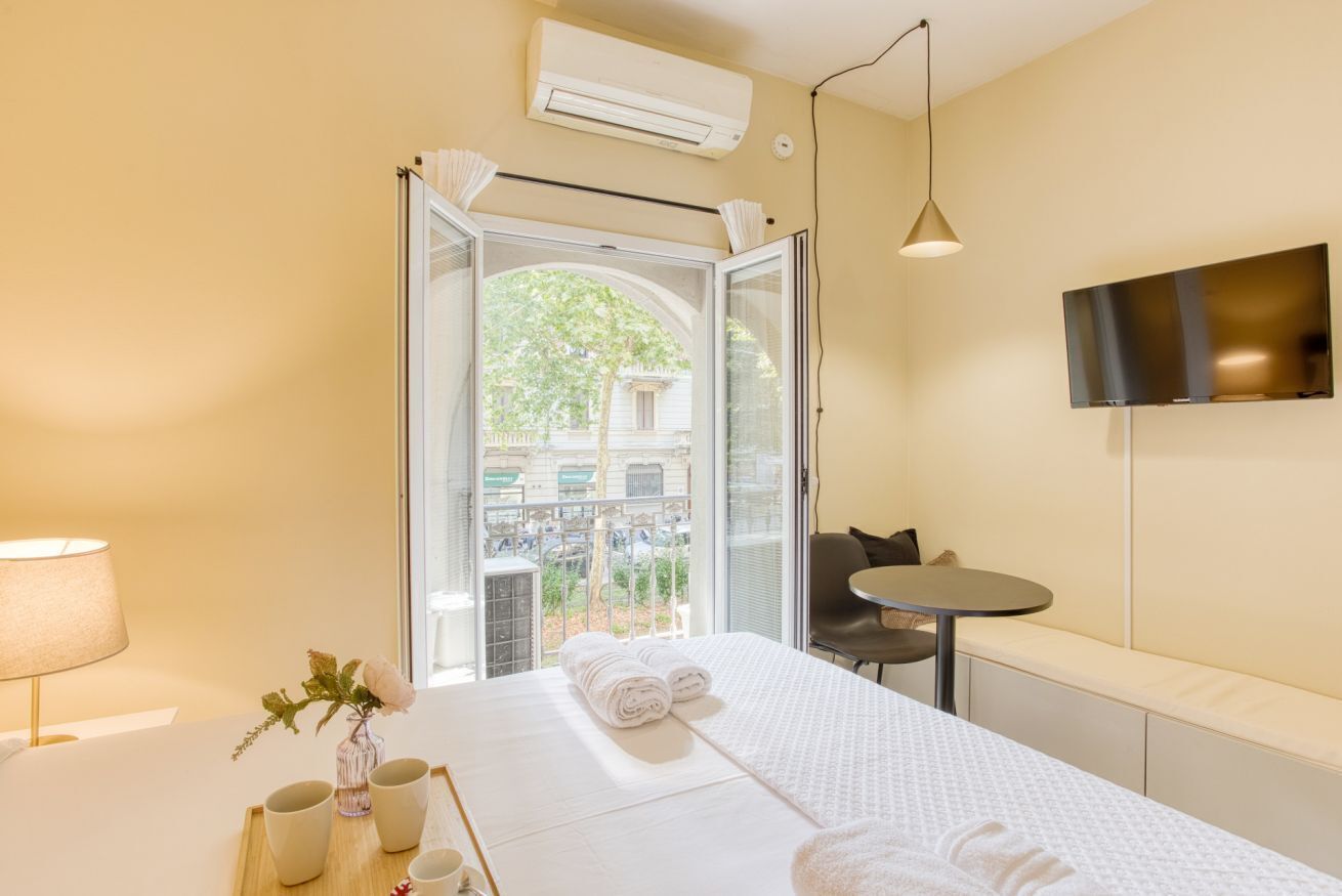 Ein Hotelzimmer mit Bett, kleinem Tisch, Fernseher und einem Balkon mit Blick auf die Stadt.