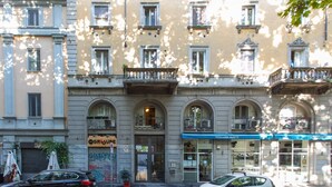 A building with multiple stories, featuring arched windows and balconies. There are parked cars in front, and a storefront with signage. - Easylife - Studio with balcony in Porta Romana (Milano)