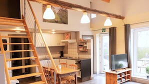 A modern kitchen with wooden cabinets, a dining area with a wooden table and chairs, a TV on a wooden stand, and a staircase leading to an upper level. - Cozy duplex apartment with terrace (Heers)