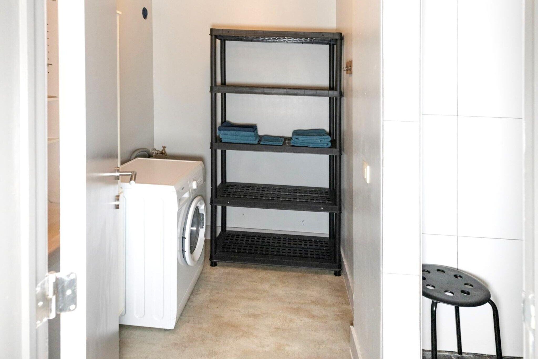 A laundry area with a washing machine, a dryer, and a black metal shelf unit with folded towels.