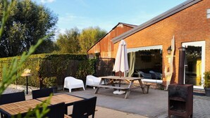 An outdoor patio with a wooden table and chairs, a white umbrella, and a brick building in the background. - Cozy duplex apartment with terrace (Heers)