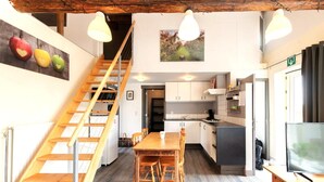 A modern kitchen with wooden cabinets, a dining table, and a staircase leading to an upper level. - Cozy duplex apartment with terrace (Heers)