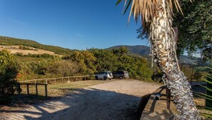 A gravel driveway leading to a parked SUV, surrounded by a fence and palm trees. - Apartment in a farmhouse with swimming pool (Assisi)
