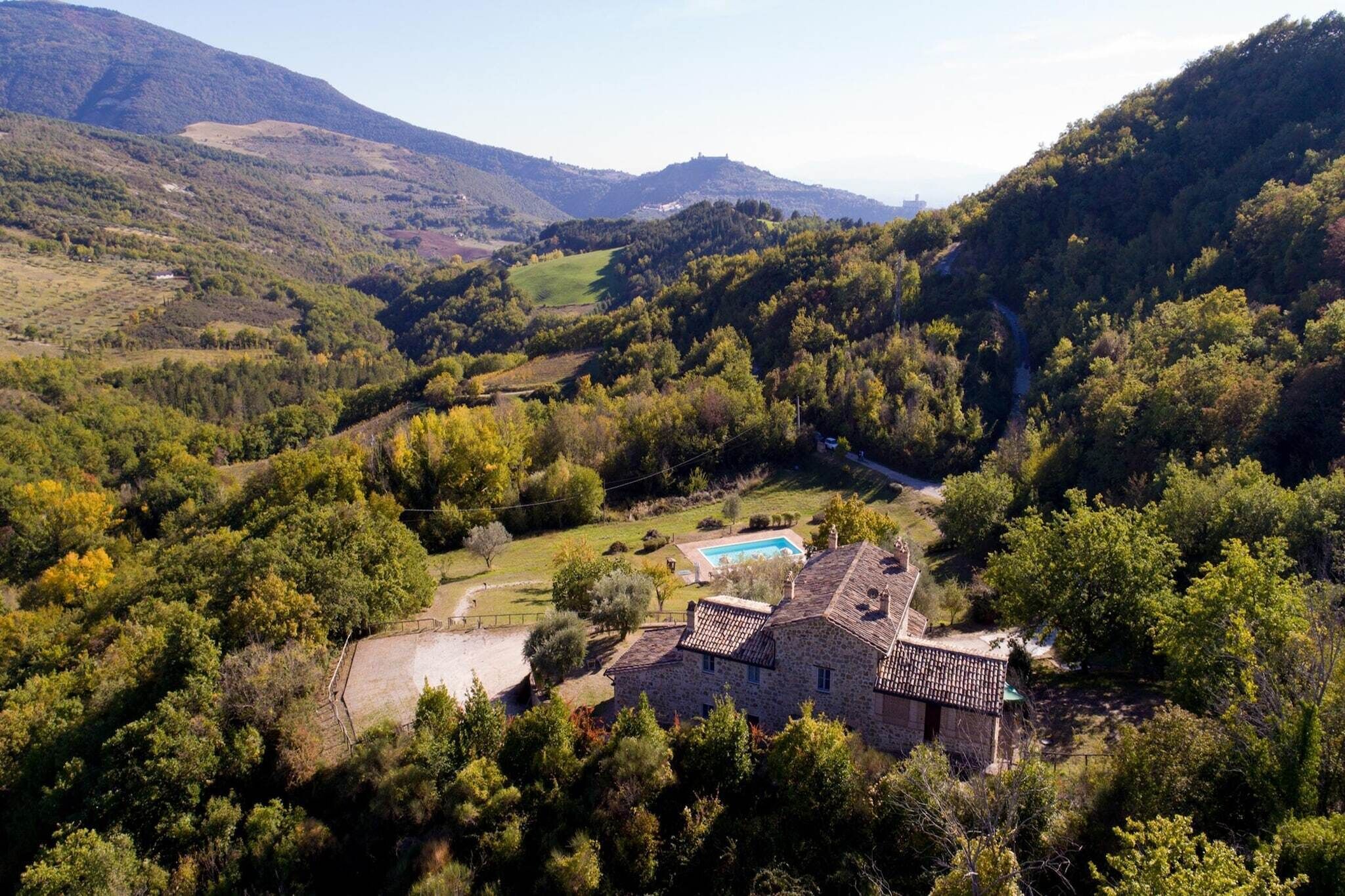 A stone house with a swimming pool surrounded by lush greenery and hills.