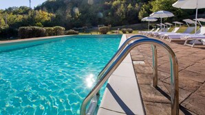 Une piscine aux eaux cristallines, dotée d’un escalier en métal, entourée de chaises longues et de parasols.