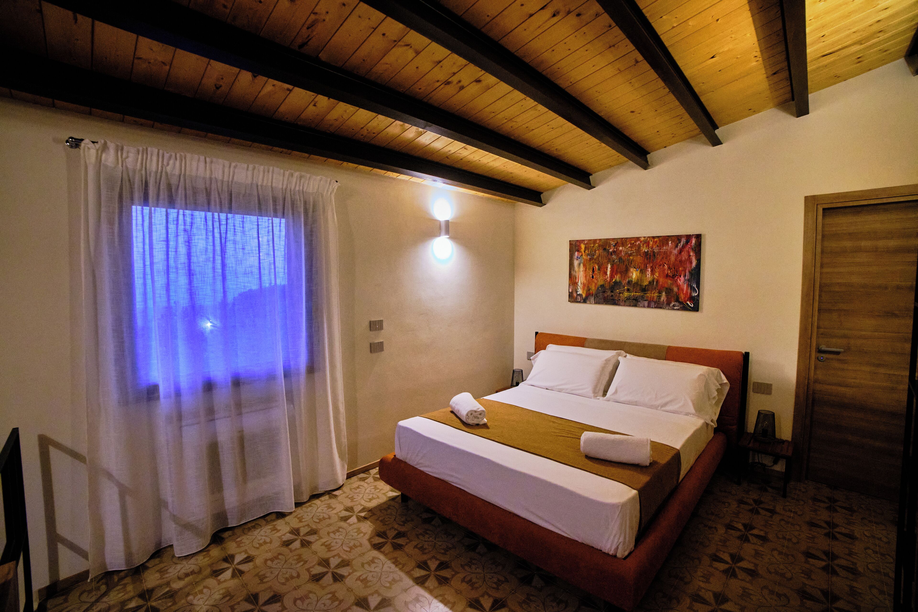 Ein Hotelzimmer mit Holzboden, einem Bett mit weißen Leinentüchern, einem Bild an der Wand und einem gemusterten Boden.