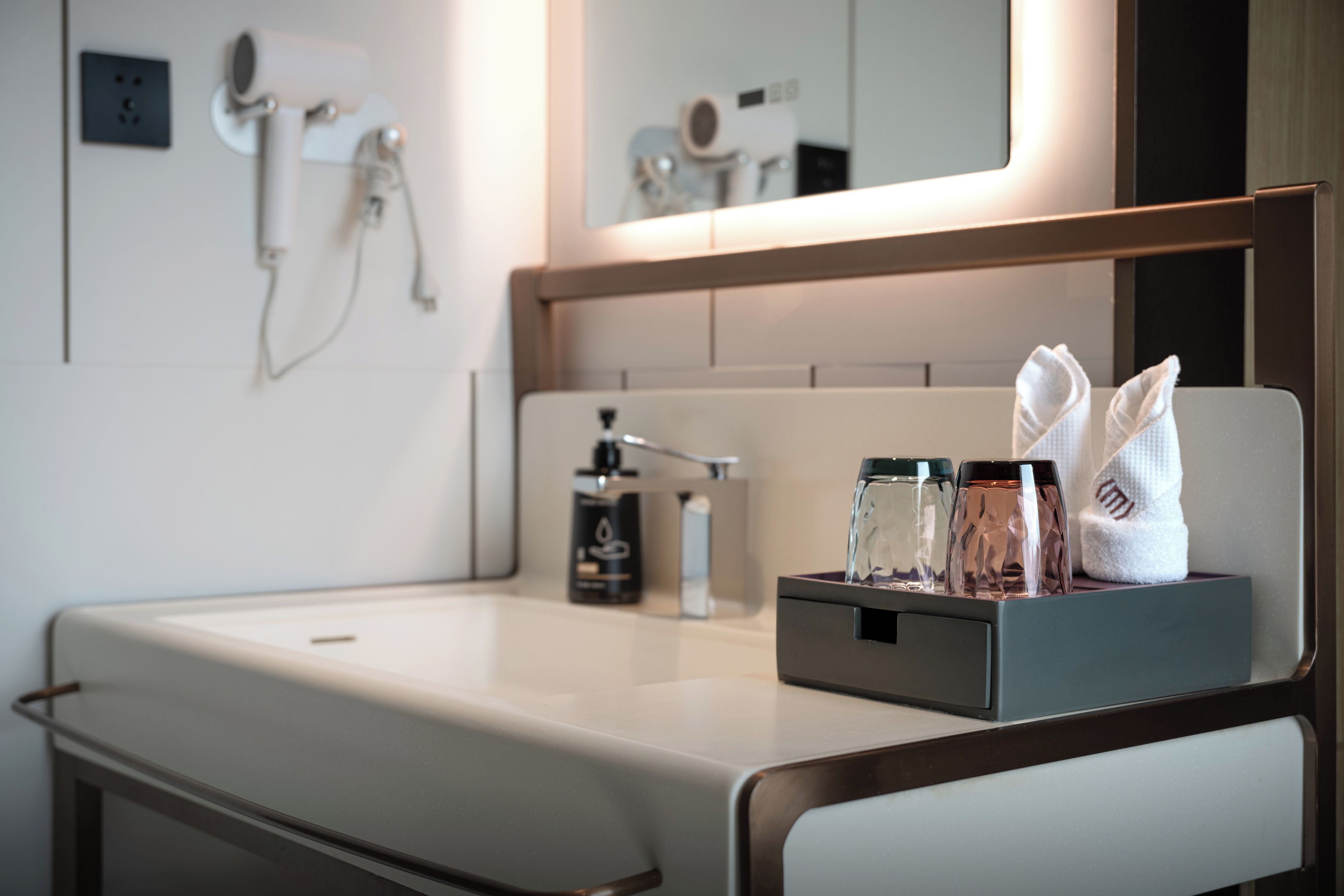 A bathroom with a sink, a mirror, and a towel dispenser.