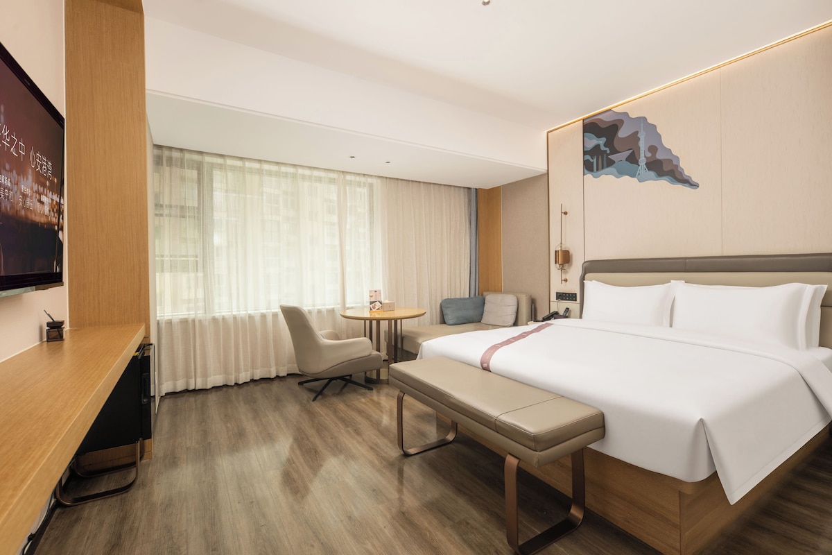 Ein Hotelzimmer mit einem Bett, einem Schreibtisch, einem Sessel, einem kleinen Tisch und einem Fernseher.