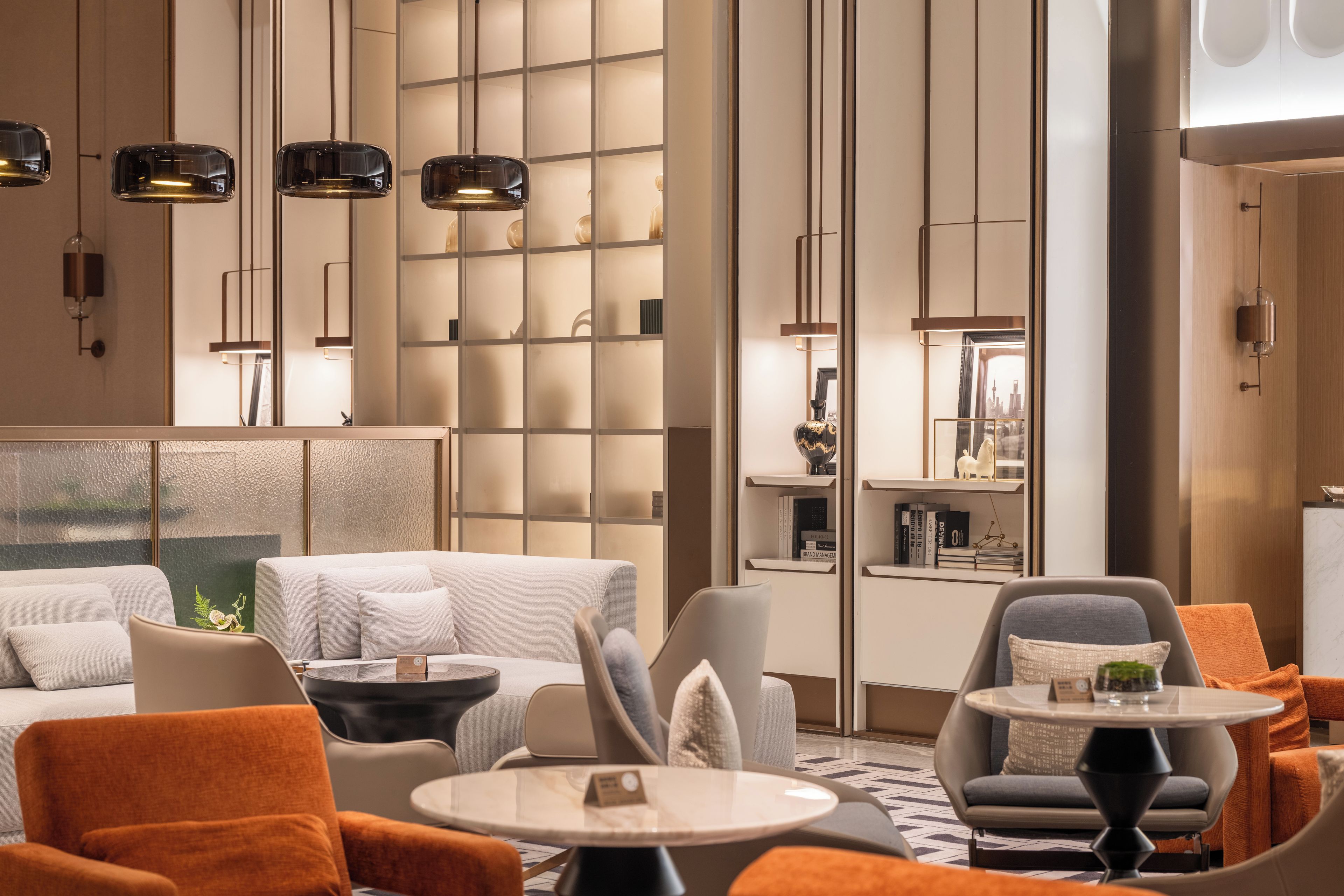 A modern hotel lobby with seating areas, a reception desk, and a decorative wall with shelves.