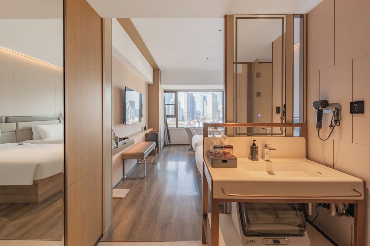 Een moderne hotelkamer met een groot bed, een bureau, een badkamer met een grote spiegel en uitzicht op de stad.