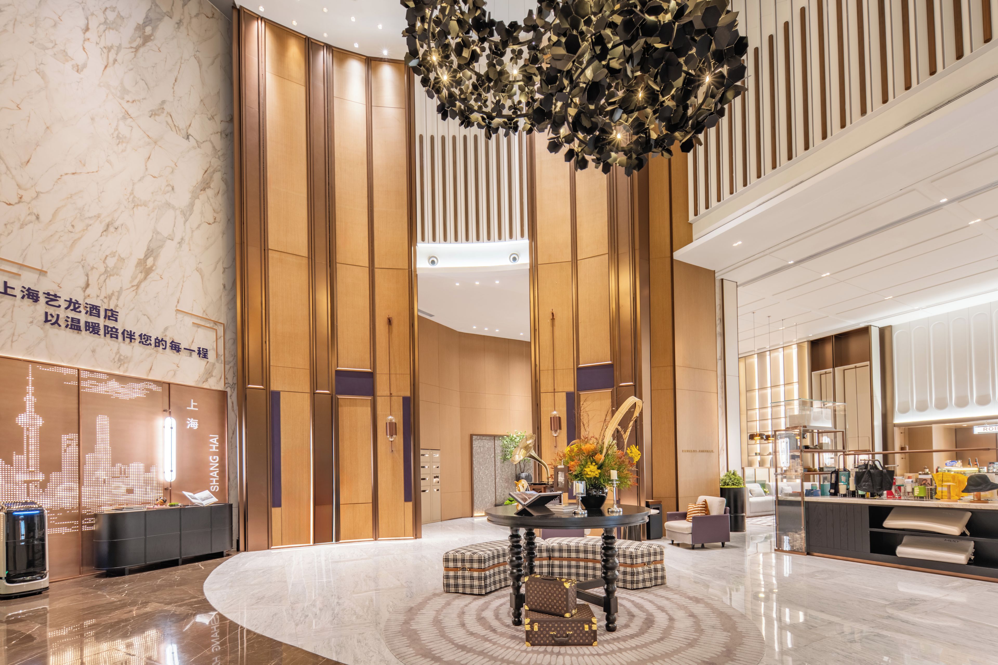 A modern hotel lobby with a central seating area, a decorative ceiling light, and a reception desk.