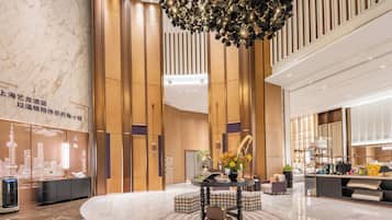A modern hotel lobby with a central seating area, a decorative ceiling light, and a reception desk.