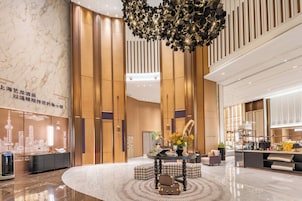 A modern hotel lobby with a central seating area, a decorative ceiling light, and a reception desk.