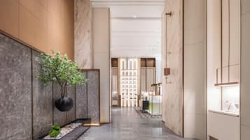 A modern hotel corridor with marble walls, a potted plant, and a display of items.