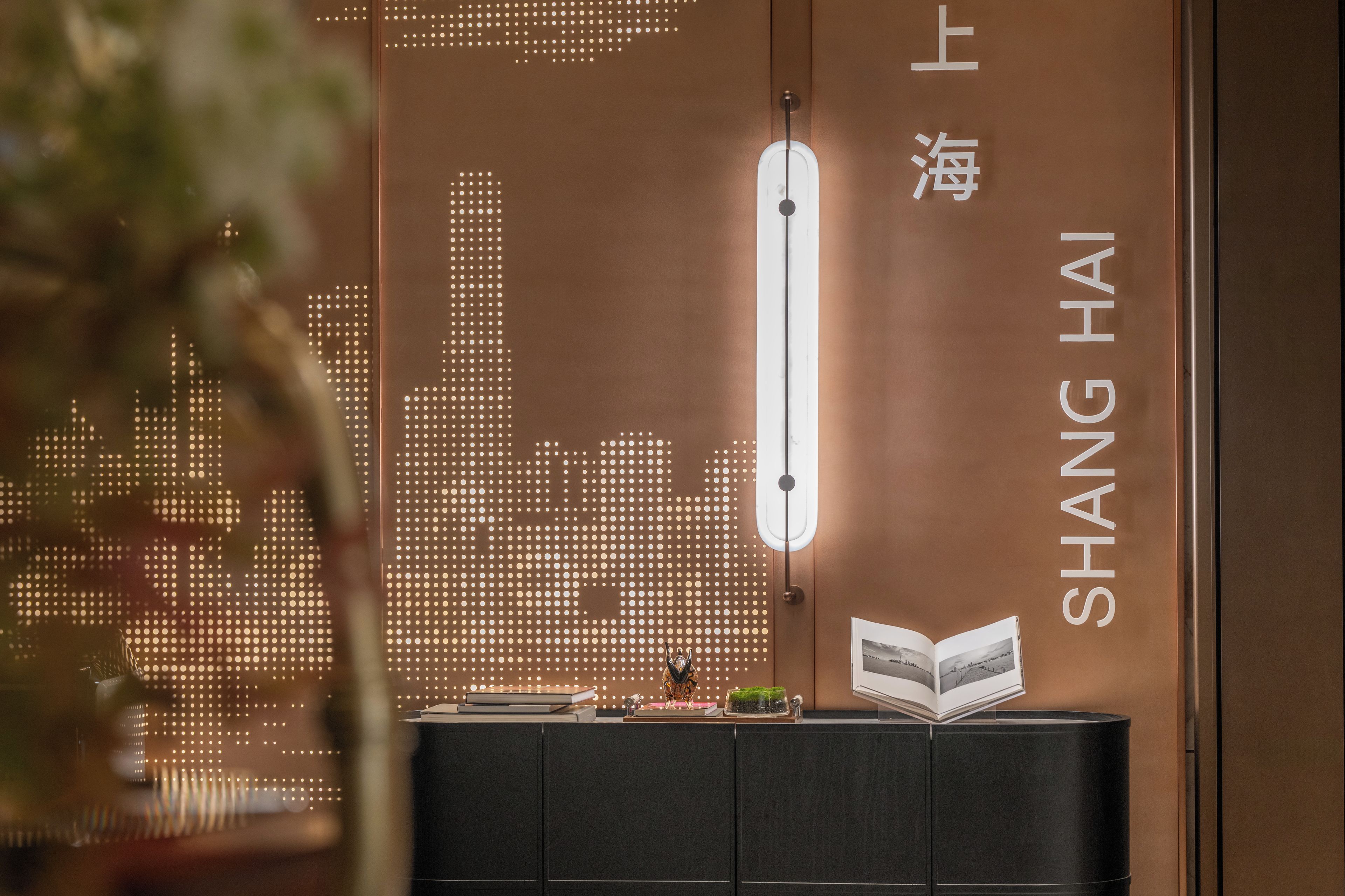 Un intérieur moderne avec un mur décoré d’un motif représentant un paysage urbain, un livre posé sur une console et un luminaire vertical.