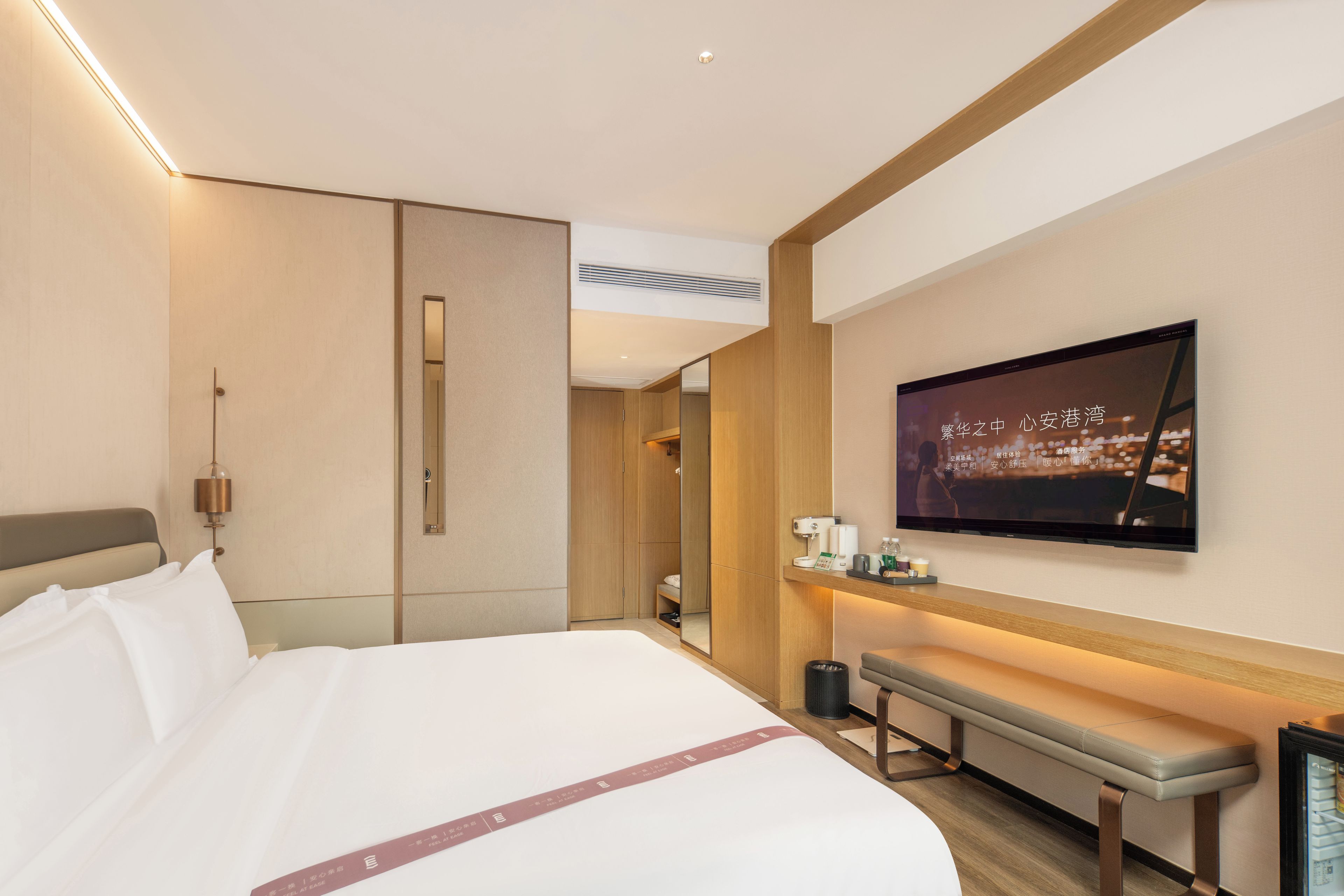 A hotel room with a large bed, a bench, a television, and a wall-mounted coffee machine.