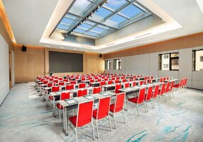 A conference room with rows of tables and chairs, a large screen, and a skylight.