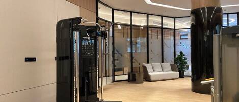 A modern office space with a glass partition, a black exercise machine, a white sofa, and a large cylindrical column.