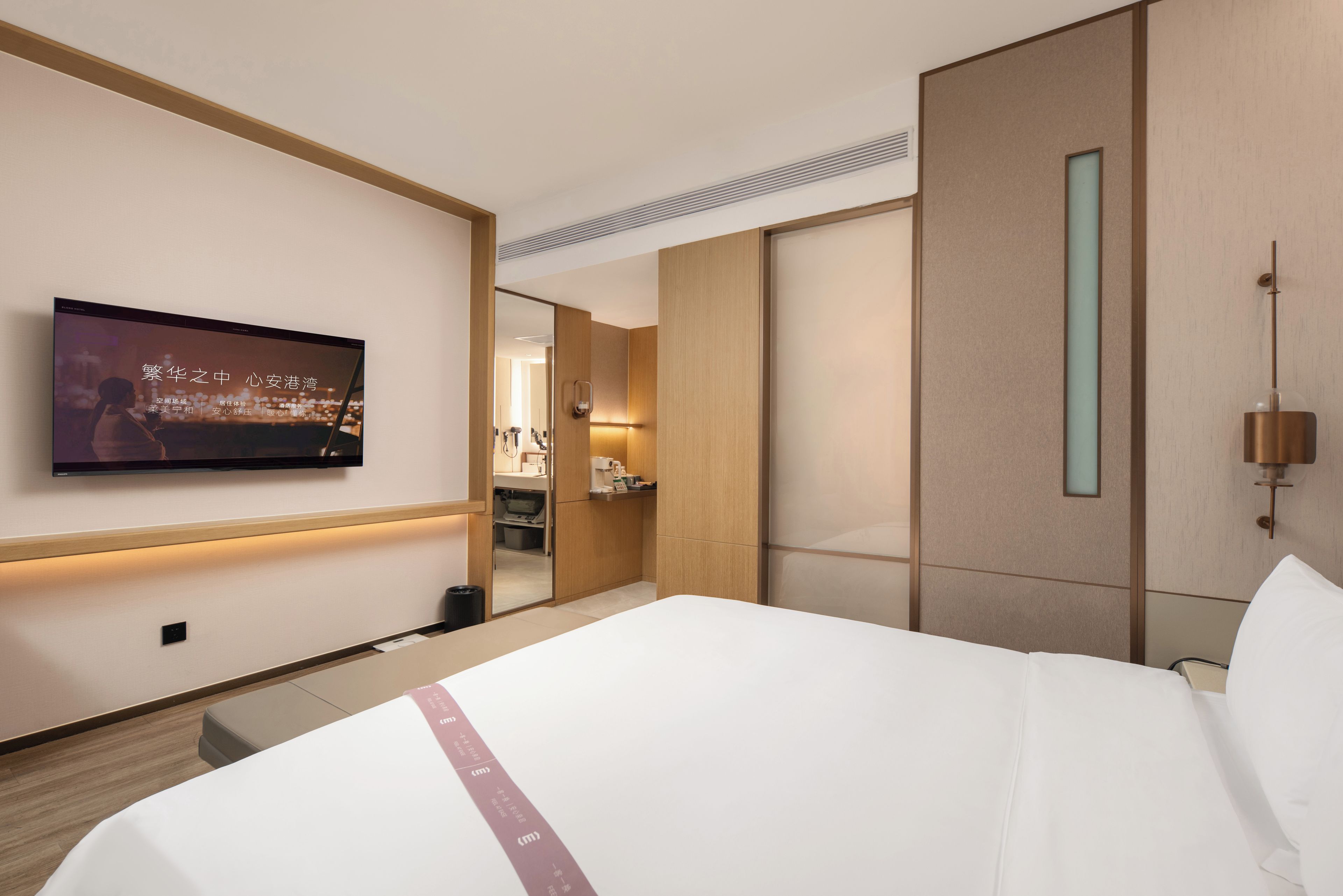 Ein Hotelzimmer mit einem Bett, einem an der Wand befestigten Fernseher, einem Spiegel und einem Nachttisch.