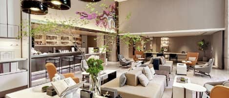 Un hall d'hôtel moderne avec un espace salon central, un bar et une cuisine en arrière-plan.