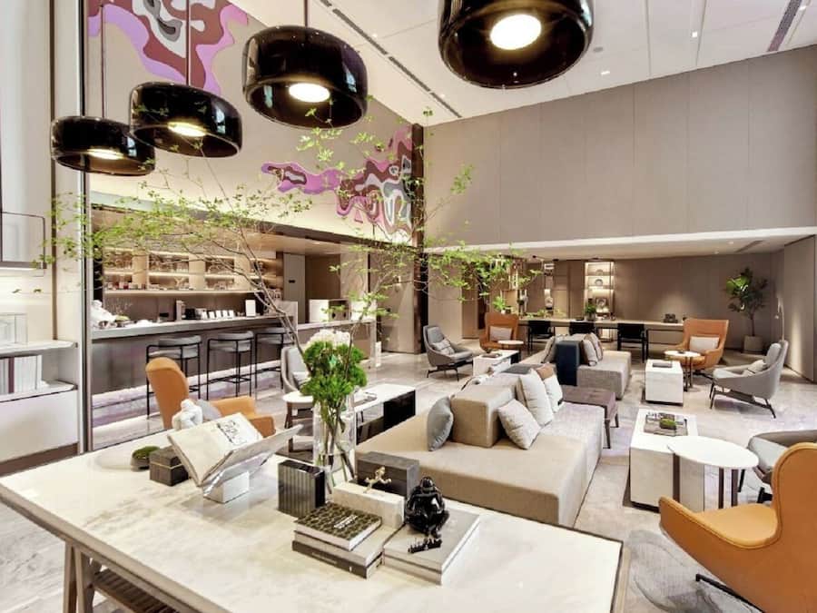 Un moderno vestíbulo de hotel con una zona de estar central, un bar y una cocina al fondo.