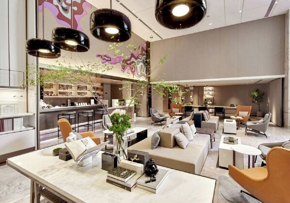 Un moderno vestíbulo de hotel con una zona de estar central, un bar y una cocina al fondo.