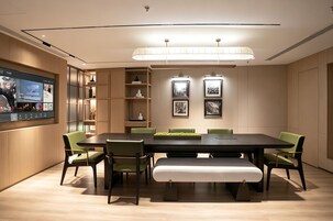 A conference room with a long table, green chairs, a bench, a TV screen, and framed pictures on the wall.