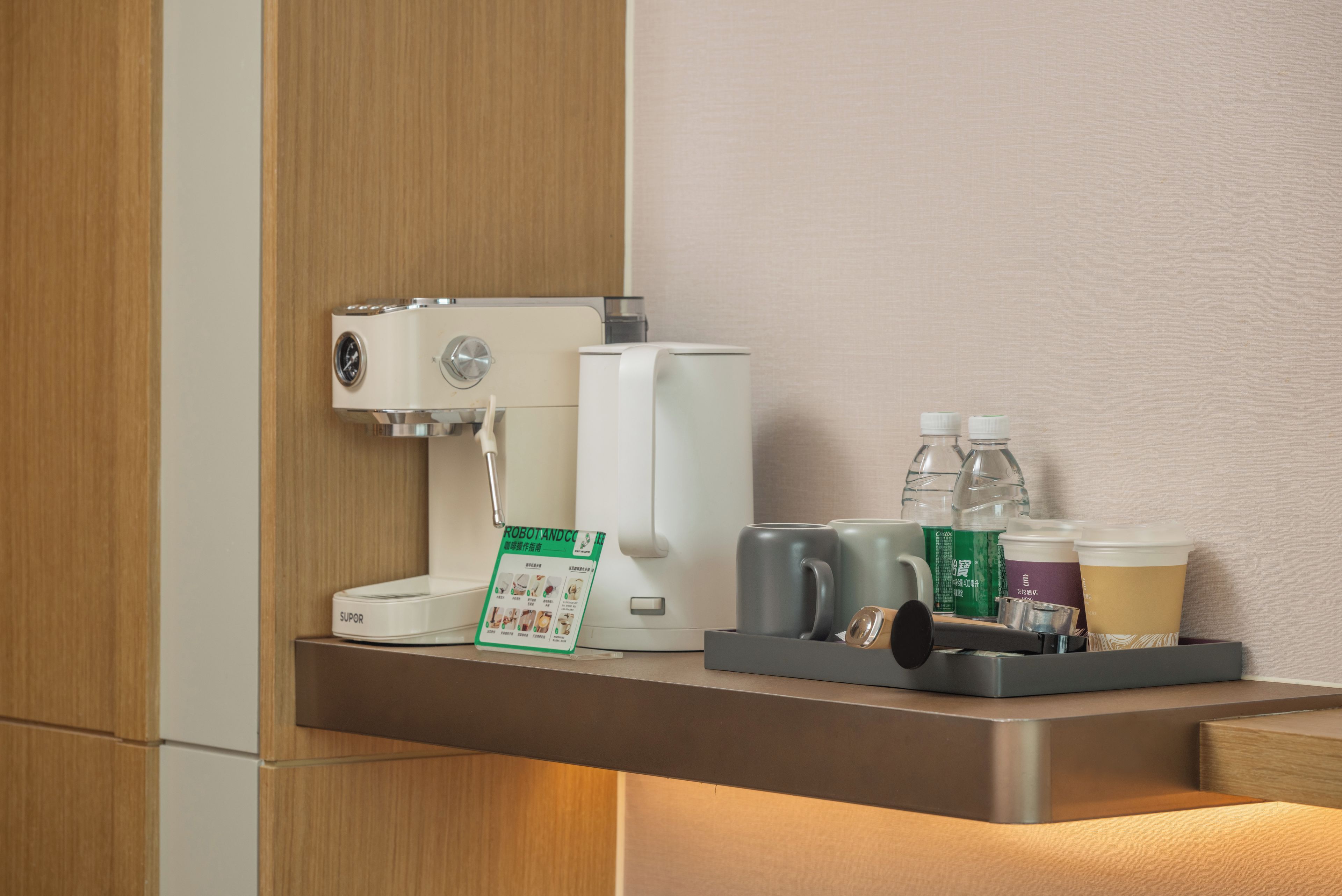 Una cafetera, botellas de agua y una bandeja con tazas y vasos sobre una encimera.