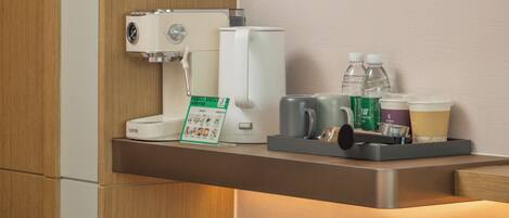 Una cafetera, botellas de agua y una bandeja con tazas y vasos sobre una encimera.