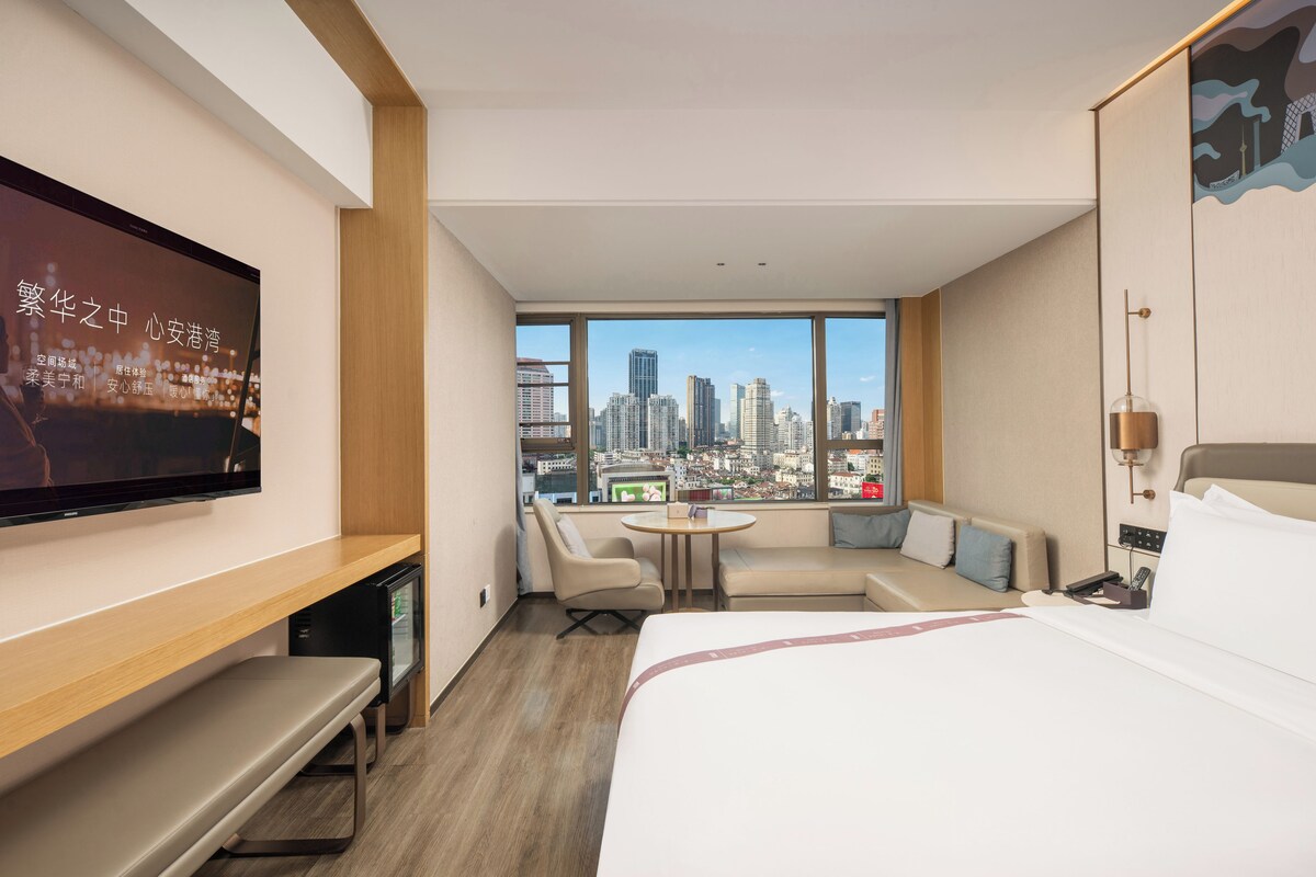 Ein Hotelzimmer mit Bett, Schreibtisch, Stuhl, kleinem Tisch und einem an der Wand befestigten Fernseher.