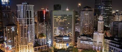 A cityscape at night with illuminated buildings, including a prominent hotel with a dome and a modern skyscraper.
