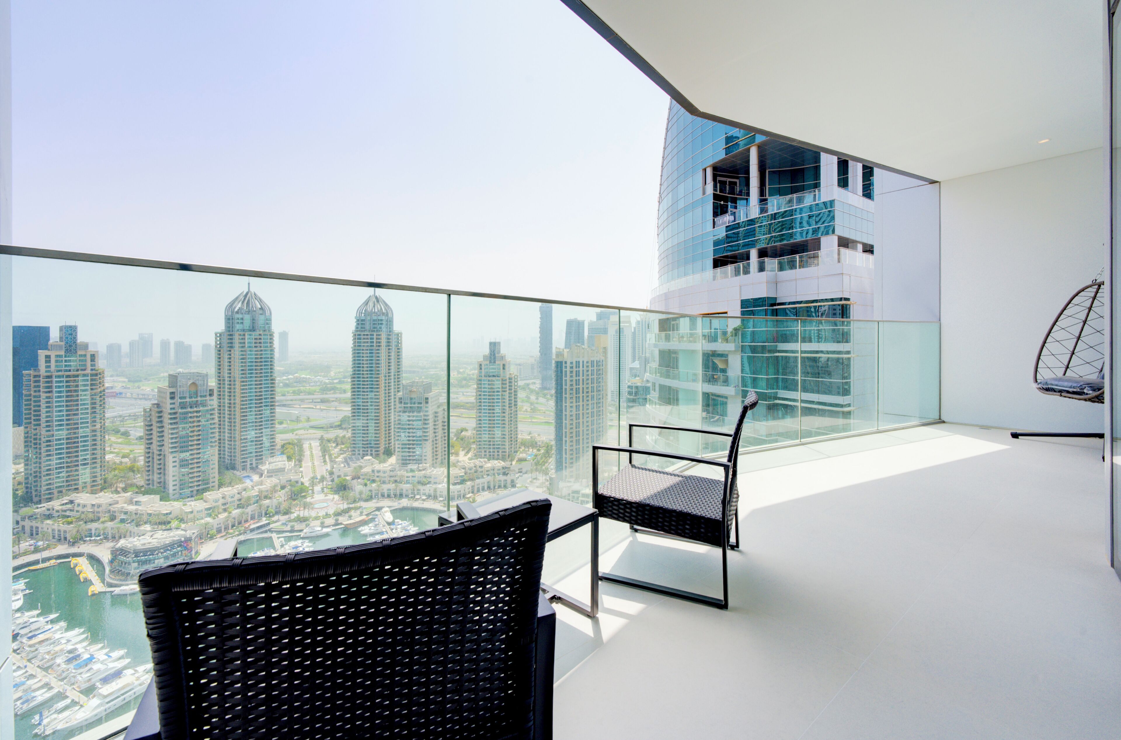 Een modern balkon met uitzicht over de stad, met twee zwarte rieten stoelen en een glazen hekwerk.