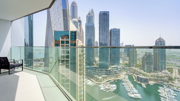 Ein Hochhaus mit einem Glasbalkon mit Blick auf eine Marina, in der Boote liegen, und eine Stadtansicht.