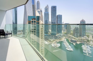 A high-rise building with a glass balcony overlooking a marina with boats and a city skyline.