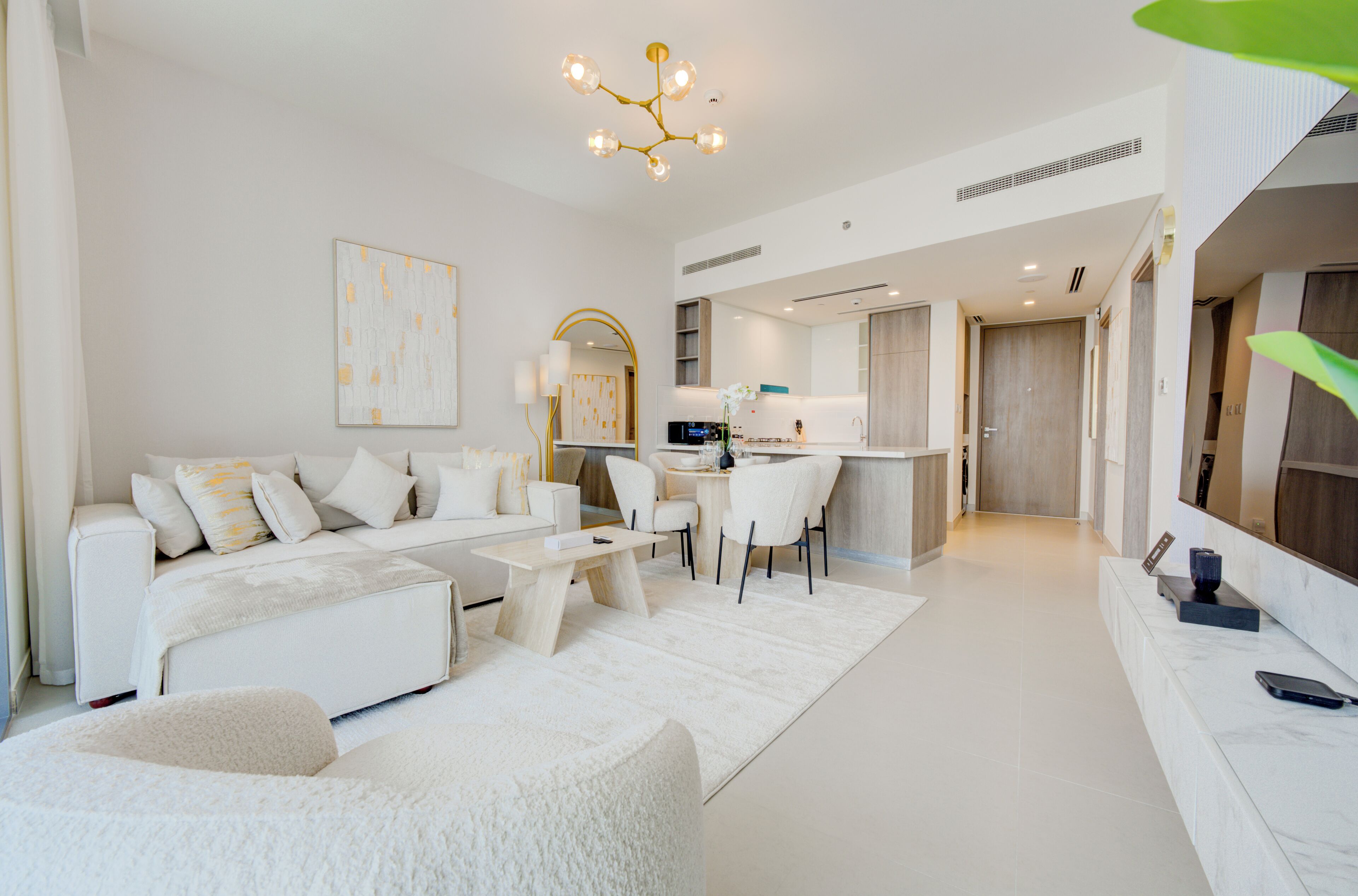 A modern living room with a sofa, coffee table, and chairs, a kitchen area with a dining table, and a large mirror.