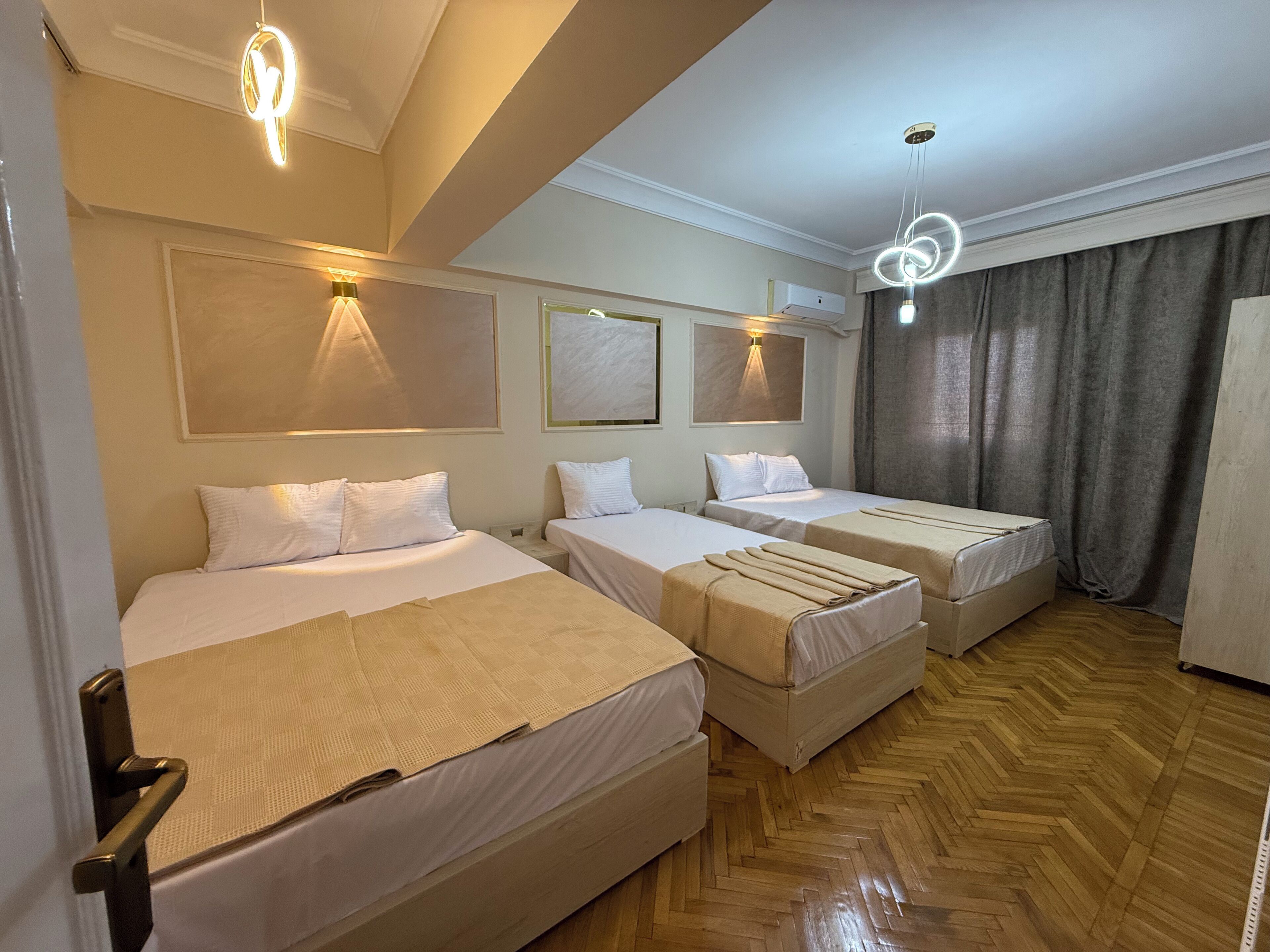 Une chambre d’hôtel avec deux lits, un parquet en bois disposé en motif chevron et un éclairage moderne à suspension.