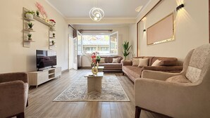 Ein Wohnzimmer mit Fernseher, Sofas, einem Couchtisch und einem großen Fenster mit Blick auf Gebäude.