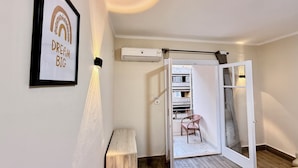 Ein Zimmer mit einem gerahmten Motivationsposter, einer Stehlampe, einer Klimaanlage, einer Schiebetür zu einem Balkon mit einem Stuhl und einem Holzboden.
