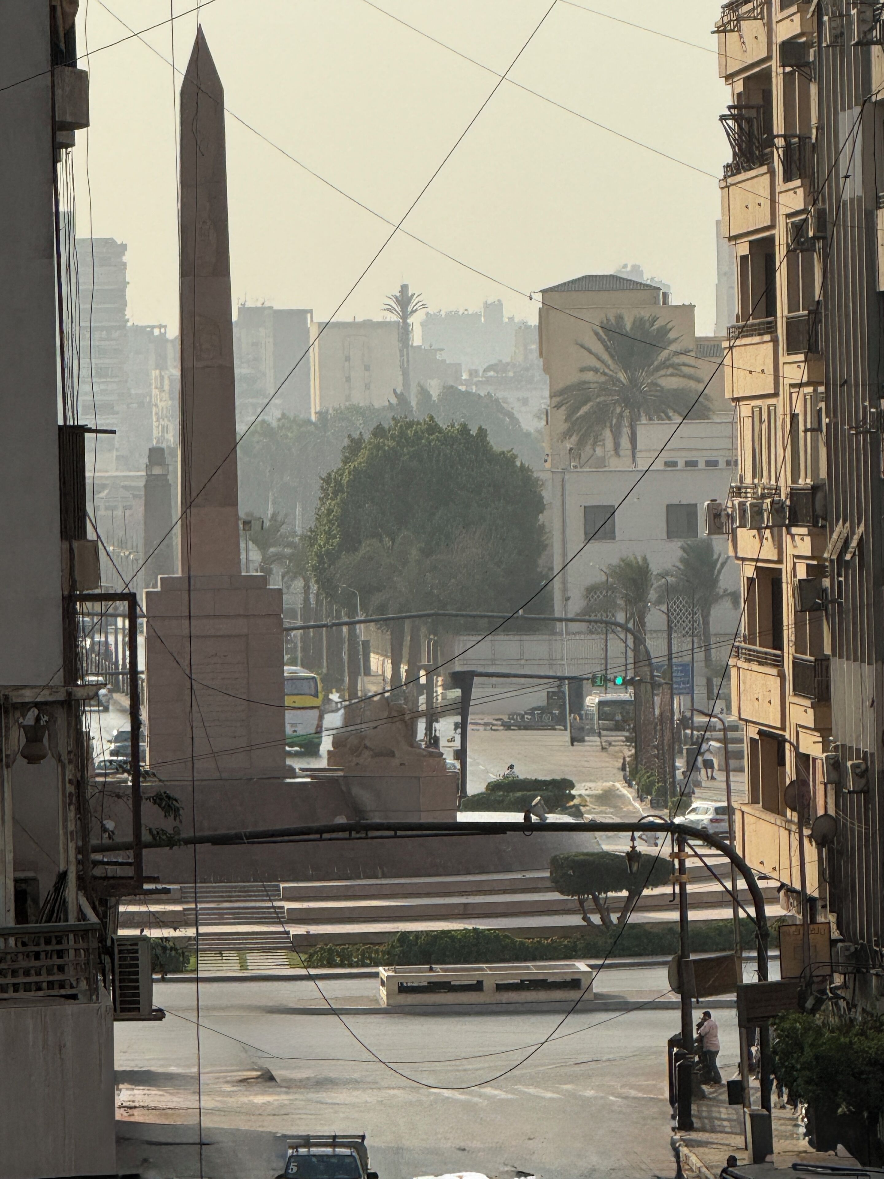 A street view with a prominent obelisk monument, buildings, and a palm tree.
