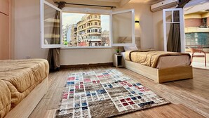 Ein Schlafzimmer mit großem Fenster, einem Bett, einem Nachttisch und Blick auf Gebäude.