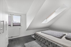 Un dormitorio con techo inclinado, una ventana, una cama y un radiador.