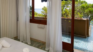 A hotel room with a bed, a window with curtains, and a view of the sea.