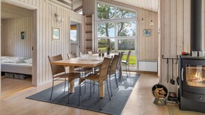 A cozy cabin interior with a dining area, a bed, and a wood-burning stove.