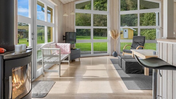 A cozy room with a fireplace, a bed, a desk, and large windows offering a view of the outdoors.