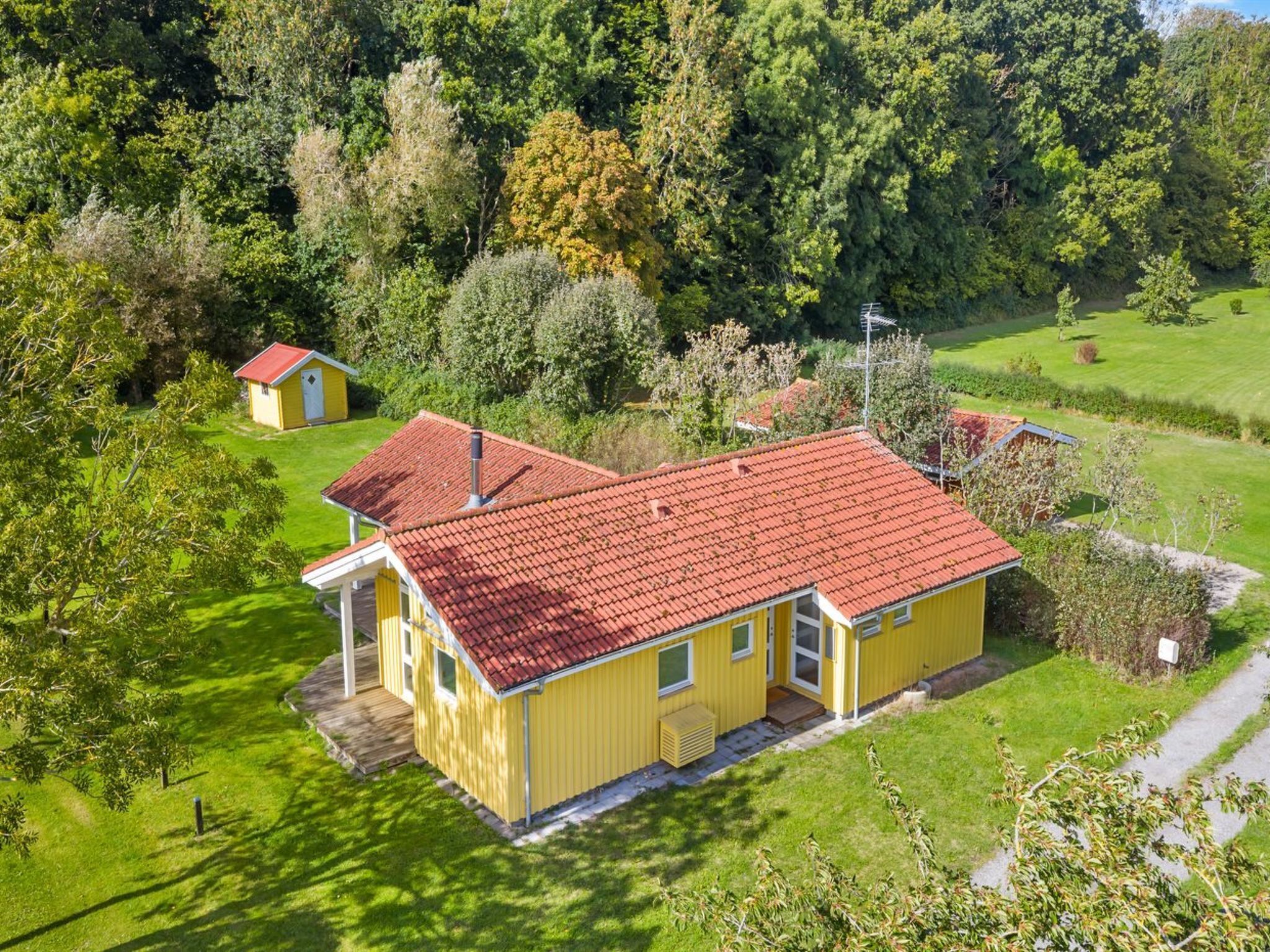 Ein gelbes Haus mit rotem Dach, umgeben von grünem Gras und Bäumen.