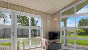 A room with a wooden bench, a TV, and large windows offering a view of the outdoors.