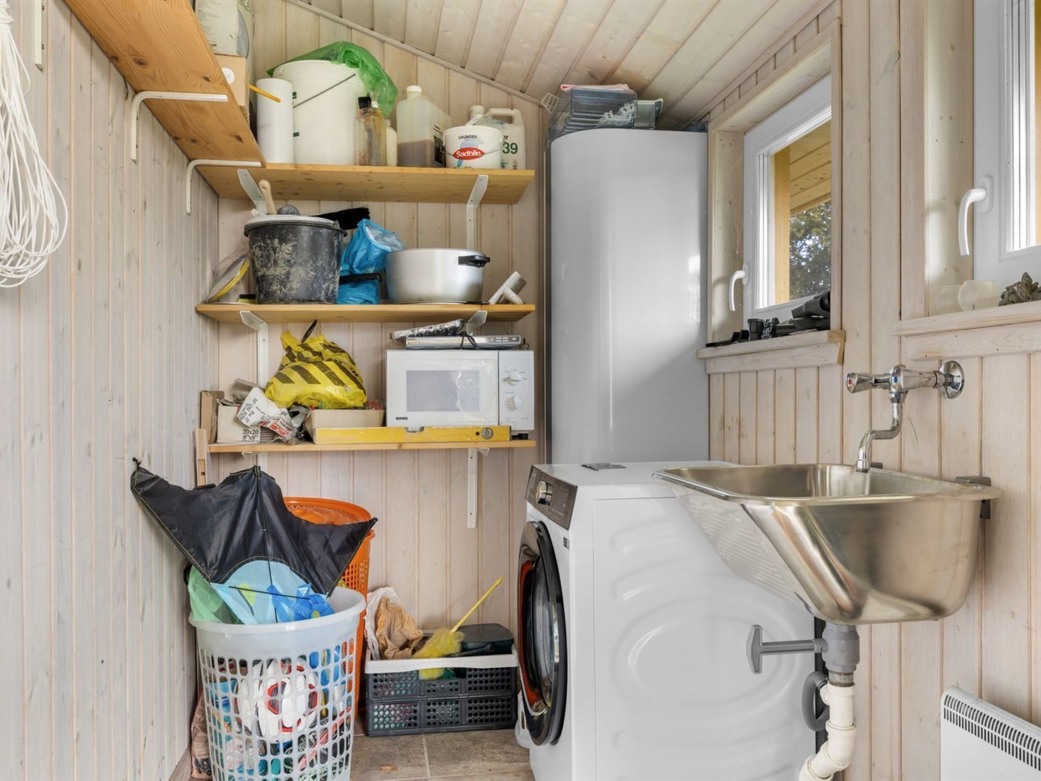 Een kleine keuken met een wasmachine, een spoelbak en diverse opbergplanken.