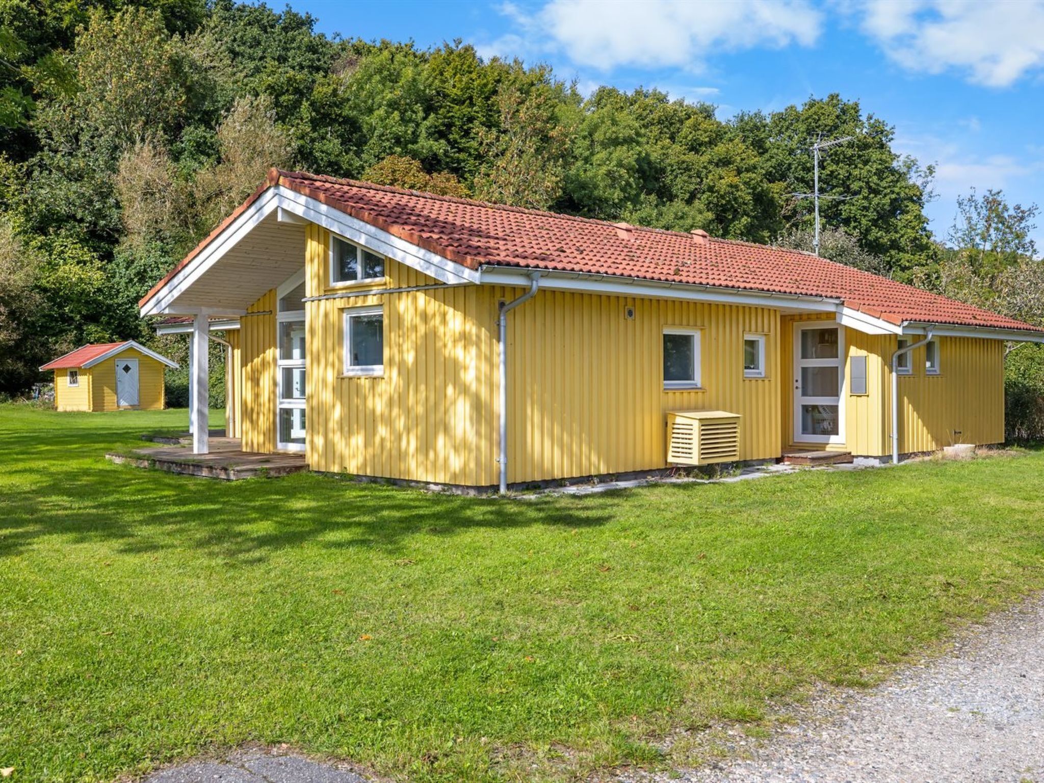 A yellow building with a red-tiled roof, a covered porch, and a small adjacent structure.